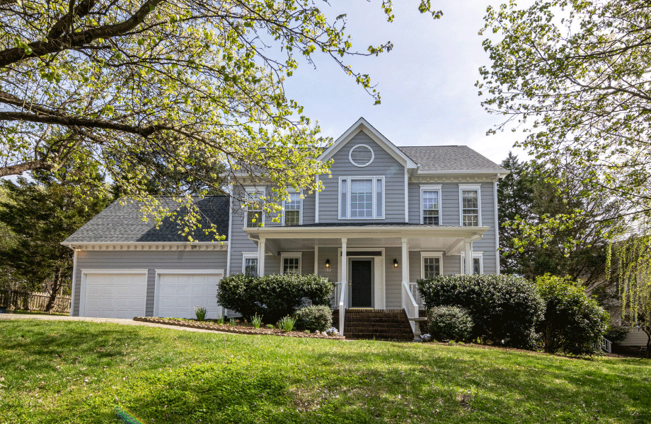 image of a beautiful grey and white house on a large sloping lawn with trees in the foreground for how to add value to your home with outdoor landscaping