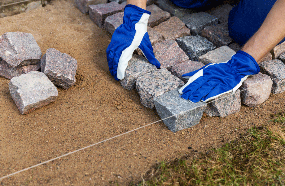 Image of a person in gloves setting pavers into a marked off cleared space of lawn for how to lay pavers in lawn