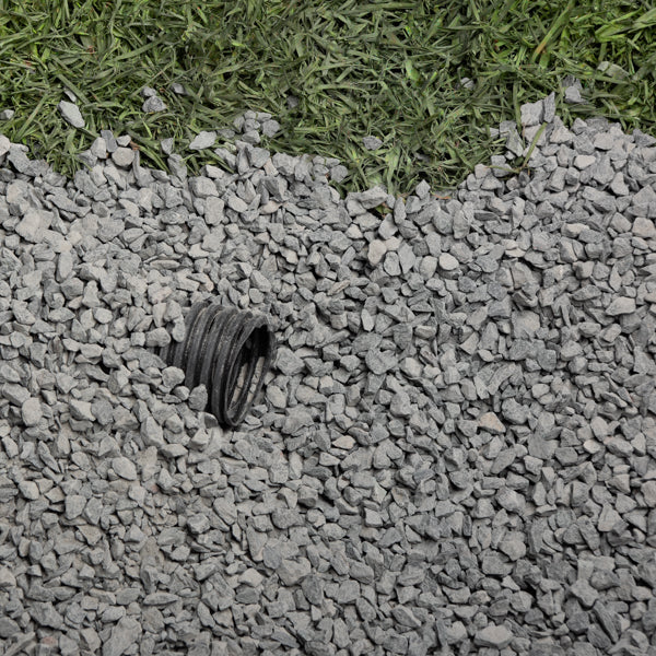 Small black pipe lying on gray gravel with green grass in the background