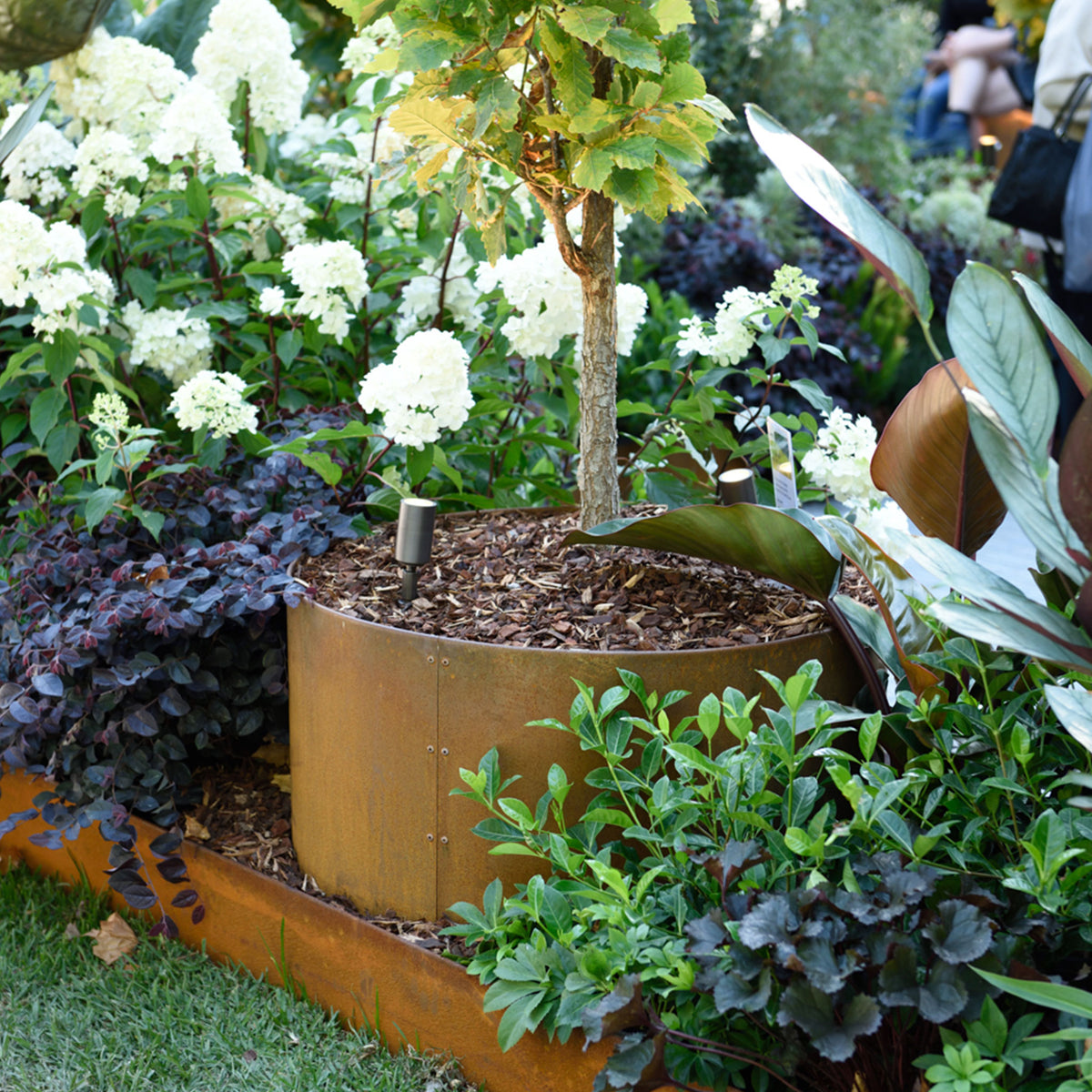 Decorative garden planter with a tree and flowers in a garden setting