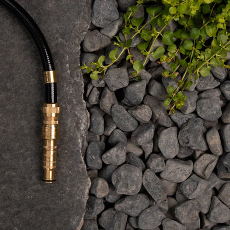 Brass garden hose fitting on a stone surface with pebbles and greenery
