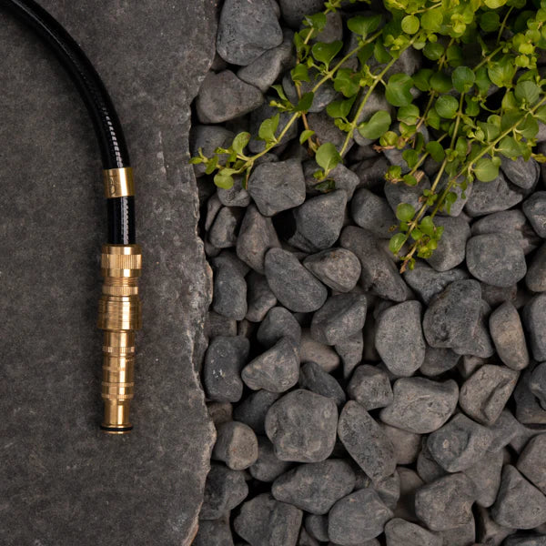 Brass garden hose fitting on a stone surface with pebbles and greenery