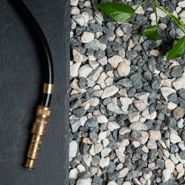 Hose with brass nozzle on a dark surface next to small stones