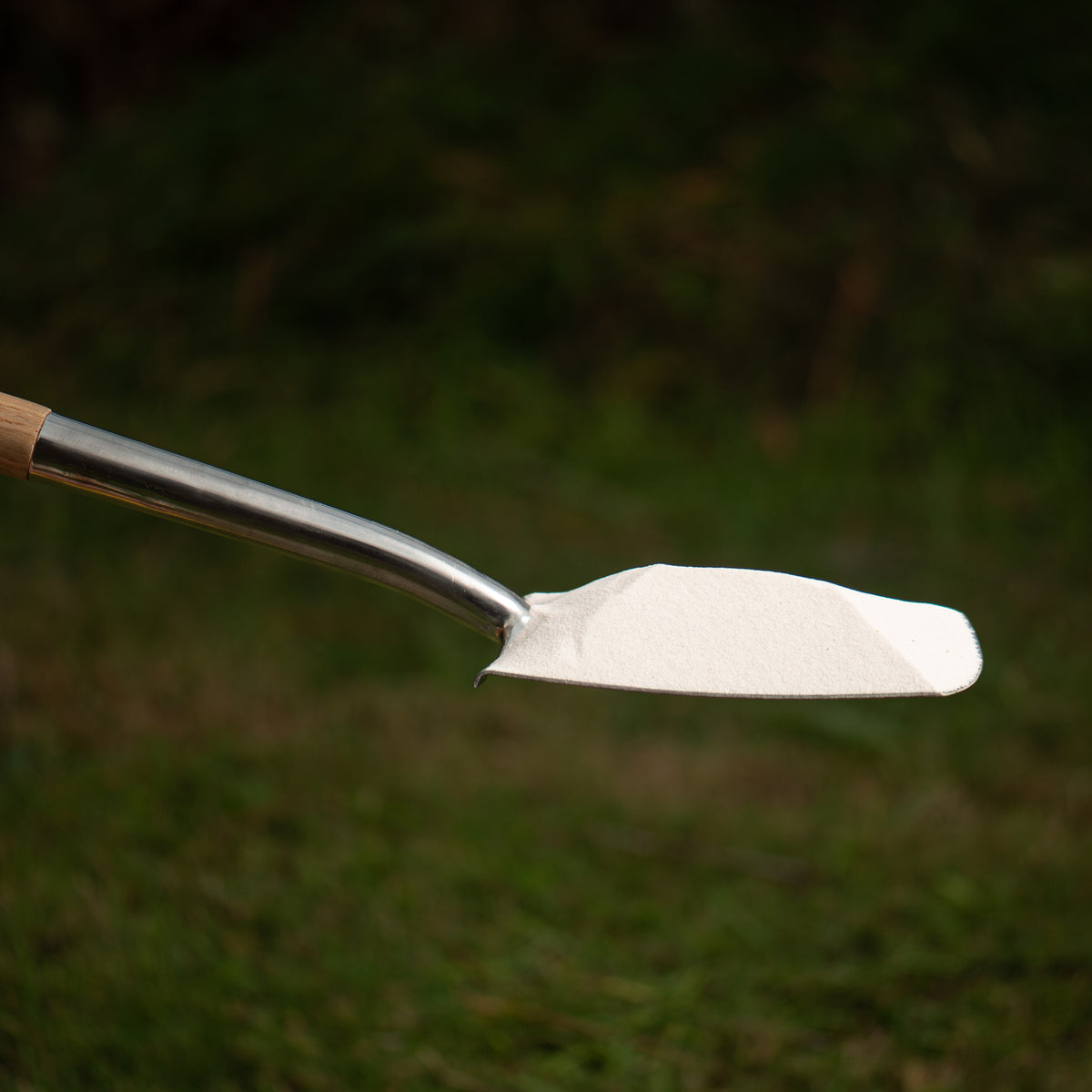 Metal garden shovel with white sand on a grassy background