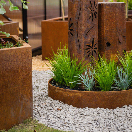 Rust-colored metal planters with green plants on a gravel surface