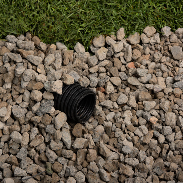 Black drain pipe embedded in small stones with grass in the background