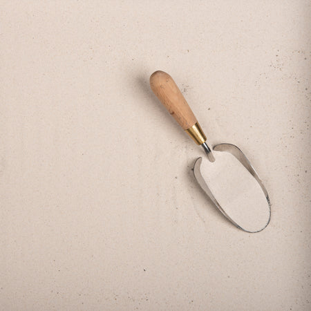 Metal garden trowel with wooden handle on a sand