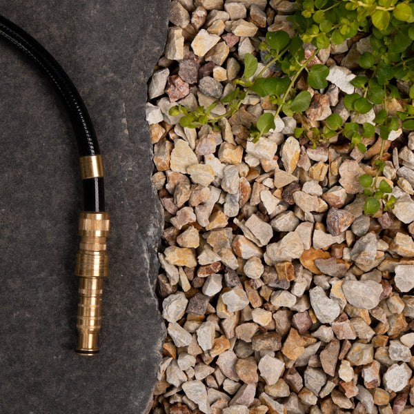 Brass garden hose nozzle on a dark surface with gravel and greenery.
