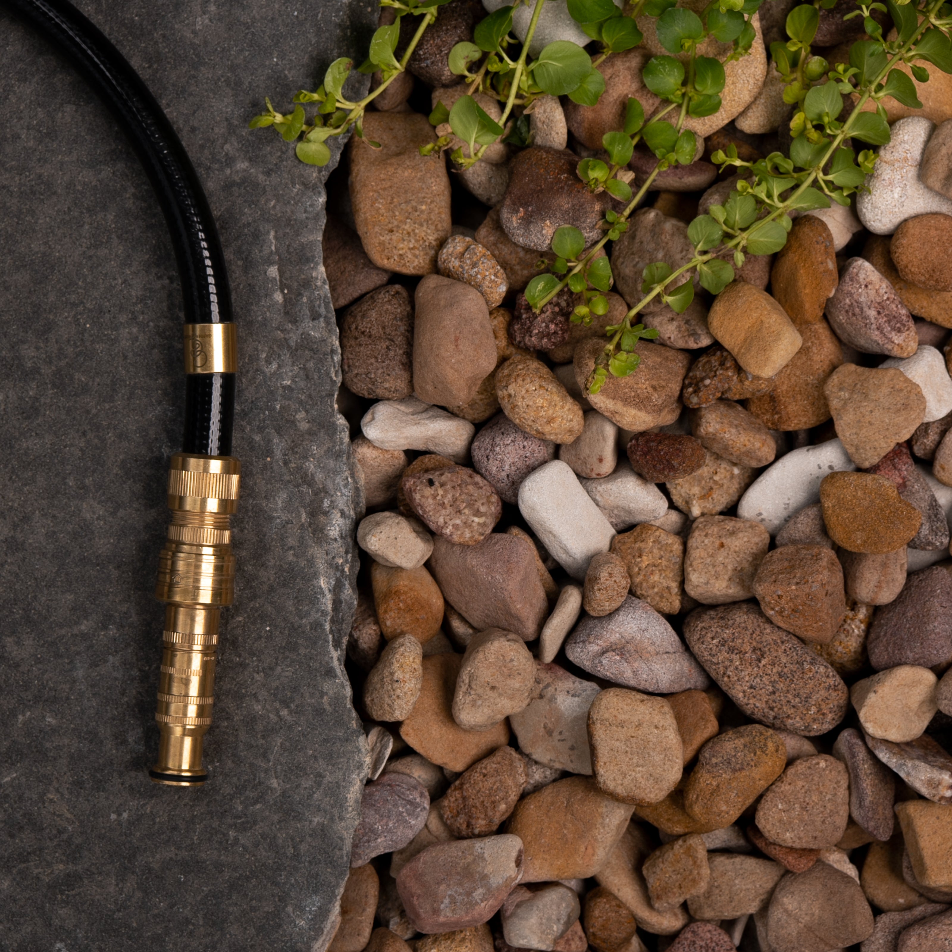 Hose with brass nozzle on a stone surface with pebbles and greenery