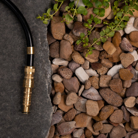 Hose with brass nozzle on a stone surface with pebbles and greenery