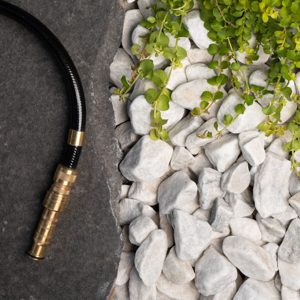 Brass garden hose nozzle on a stone surface with pebbles and greenery.