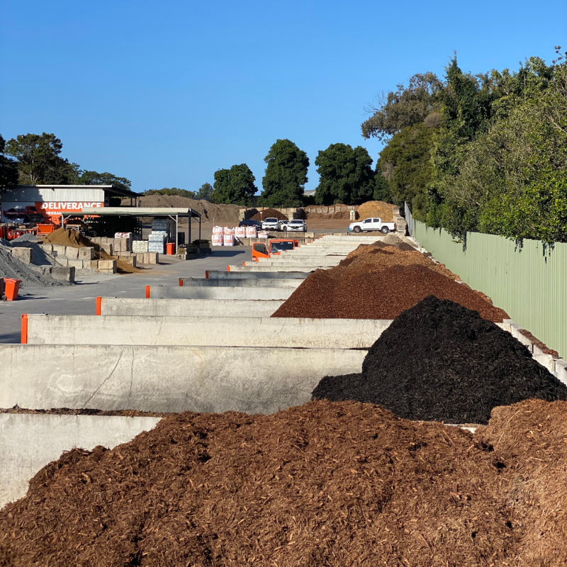 Piles of soil or compost in a construction or landscaping area with trees and buildings in the background.