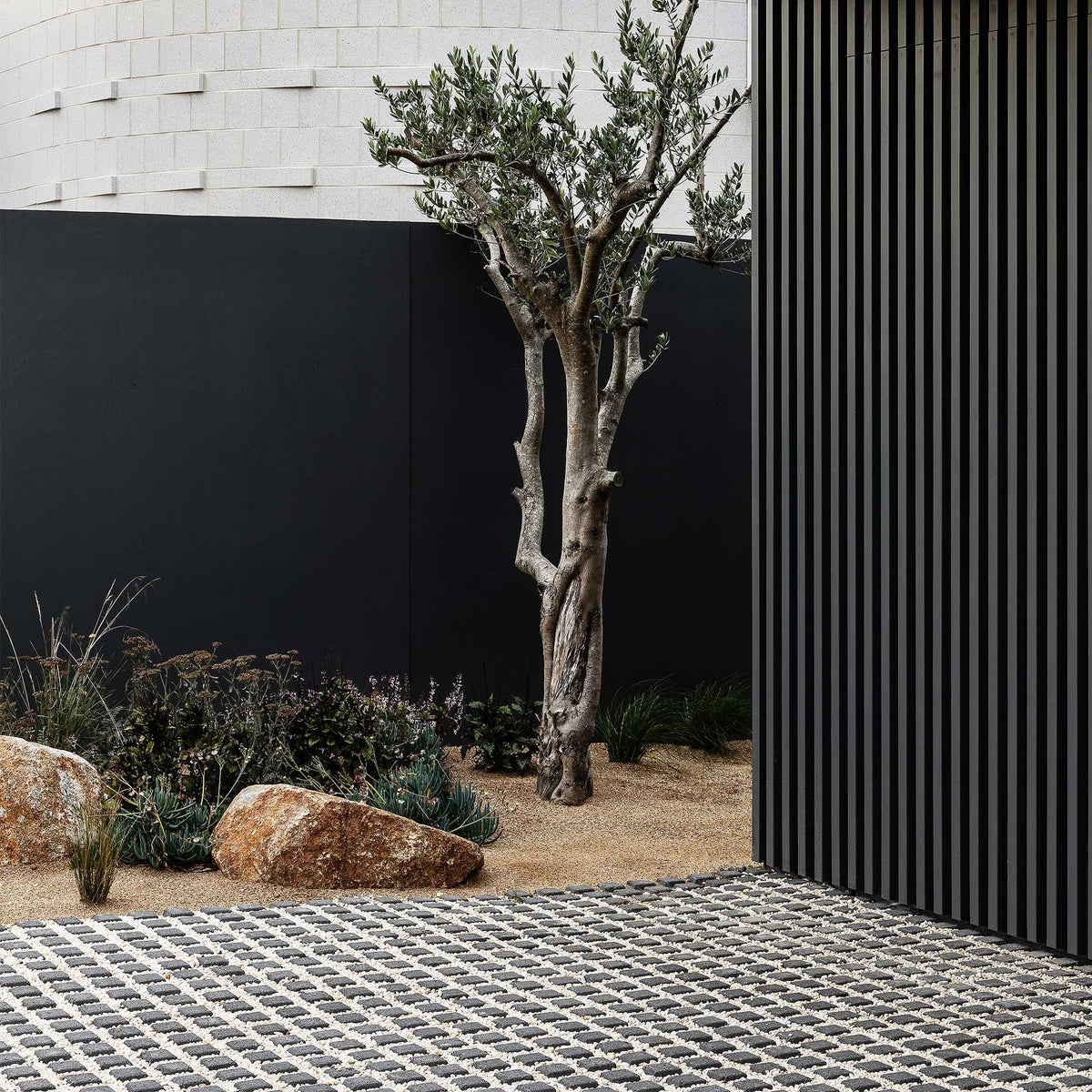 Modern outdoor setting with a tree, rocks, and a black wall.
