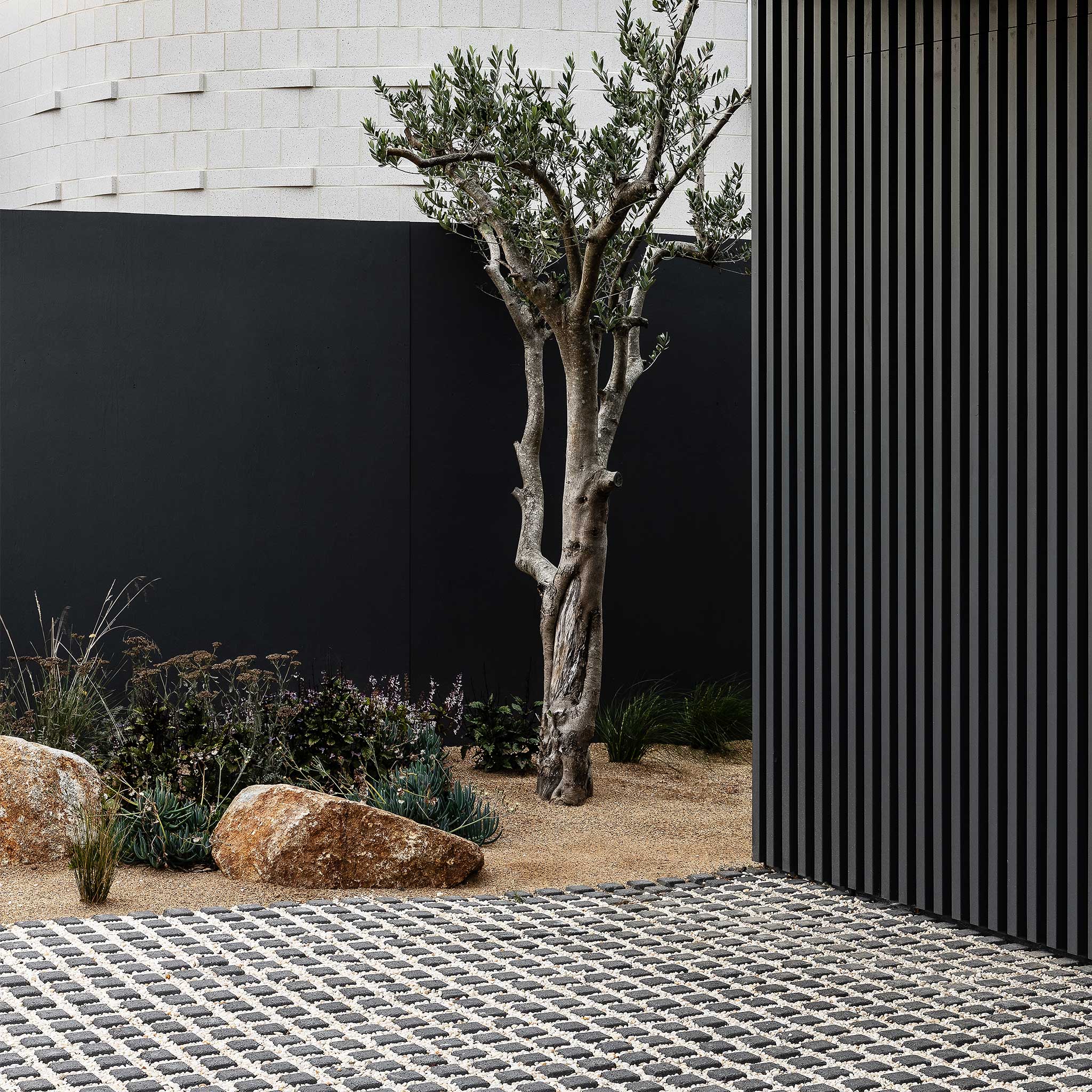 Modern outdoor setting with a tree, rocks, and a black wall.