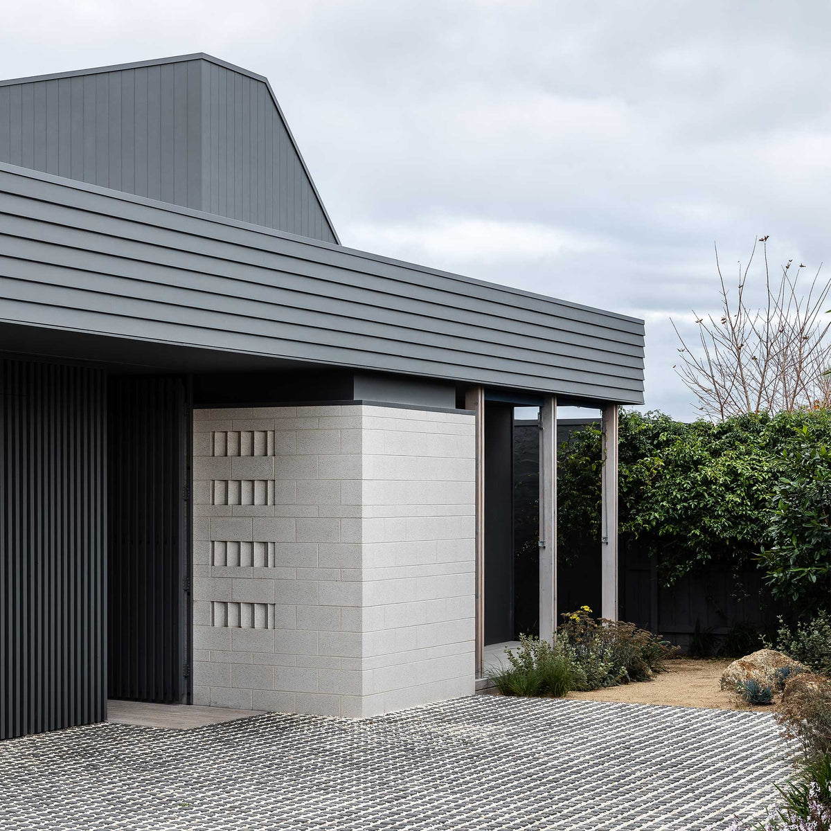 Modern house exterior with gray roof and white wall, surrounded by greenery.