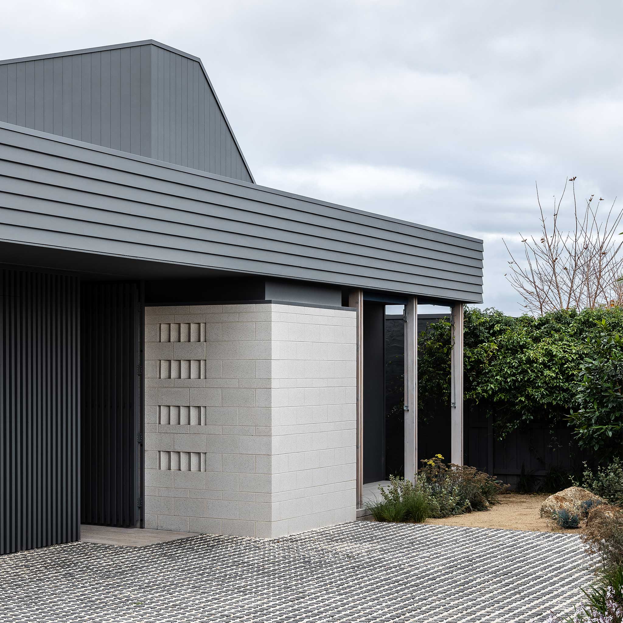Modern house exterior with gray roof and white wall, surrounded by greenery.