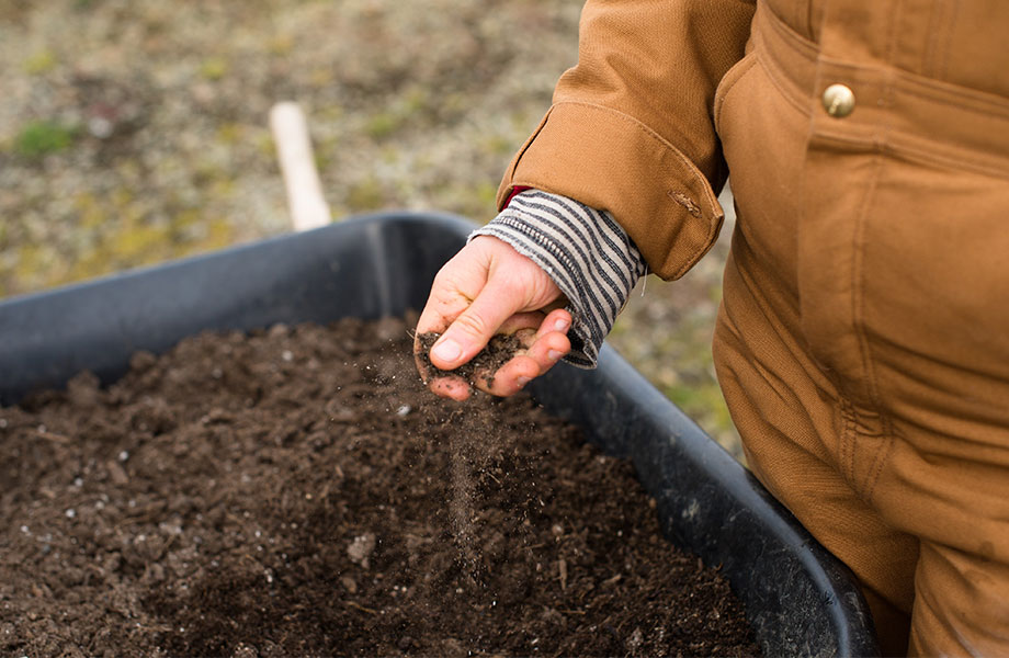 image of someone in brown coveralls feeling premium garden soil in a wheelbarrow for what soil to use