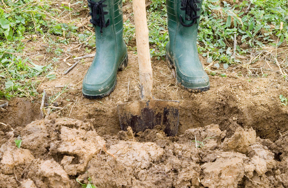 image of a landscaper in green boots digging a hole in the dirt with a shovel