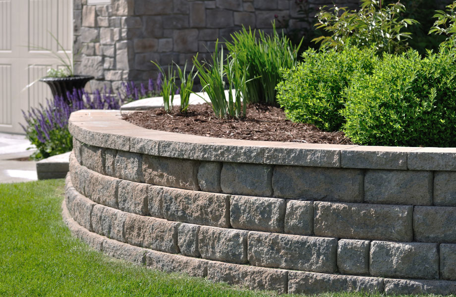 image of a curved stone retaining wall with a garden bed and a lawn beneath for masonry maintenance 