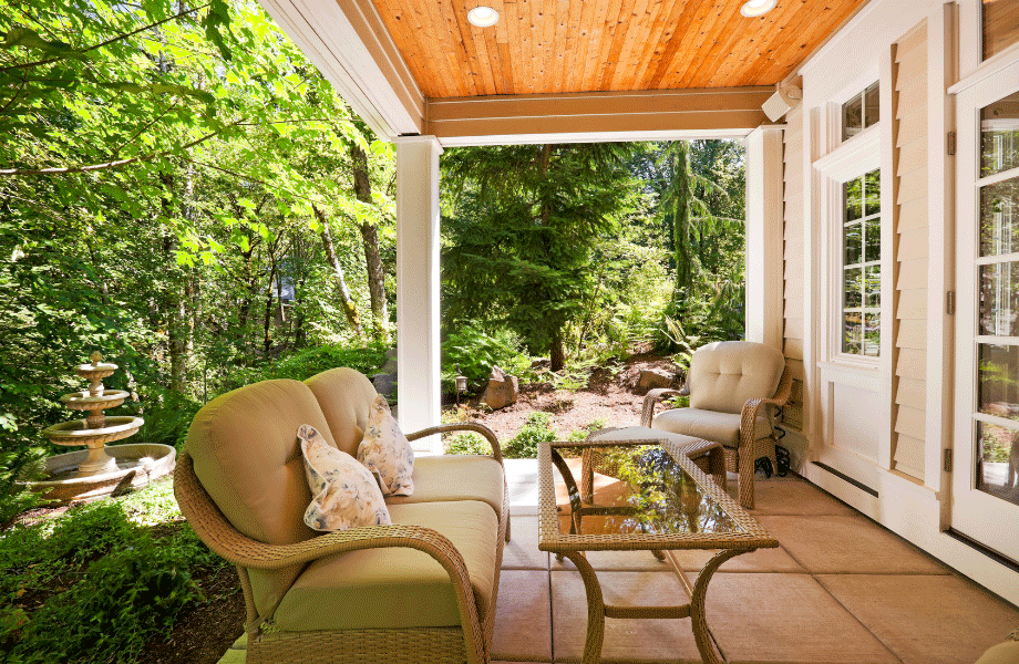 patio with lounge and chair and coffee table set amongst a lush green landscape with trees, hedges and vibrant bushes and a water feature