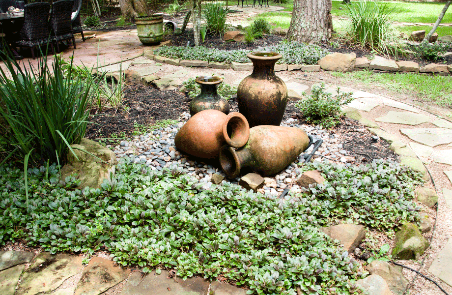 water feature centred in a garden bed with succulents surrounded by paving in the midst of a wider garden with trees, plants and stonework
