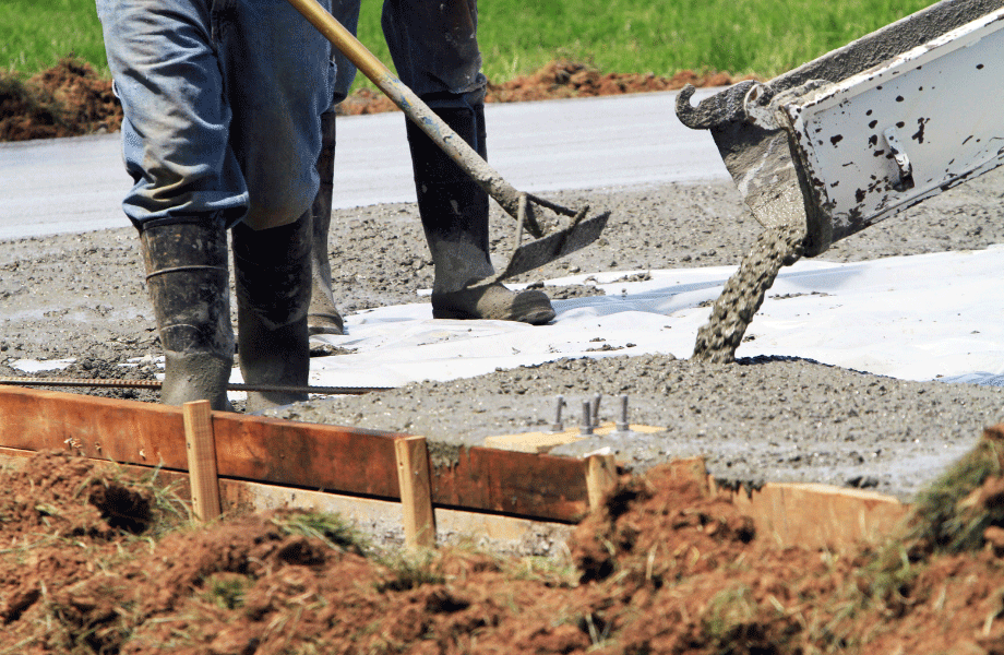 image of two people's legs only with a concrete pourer and pouring concrete and using a hoe to spread around with wooden edging in place for difference between cement and concrete